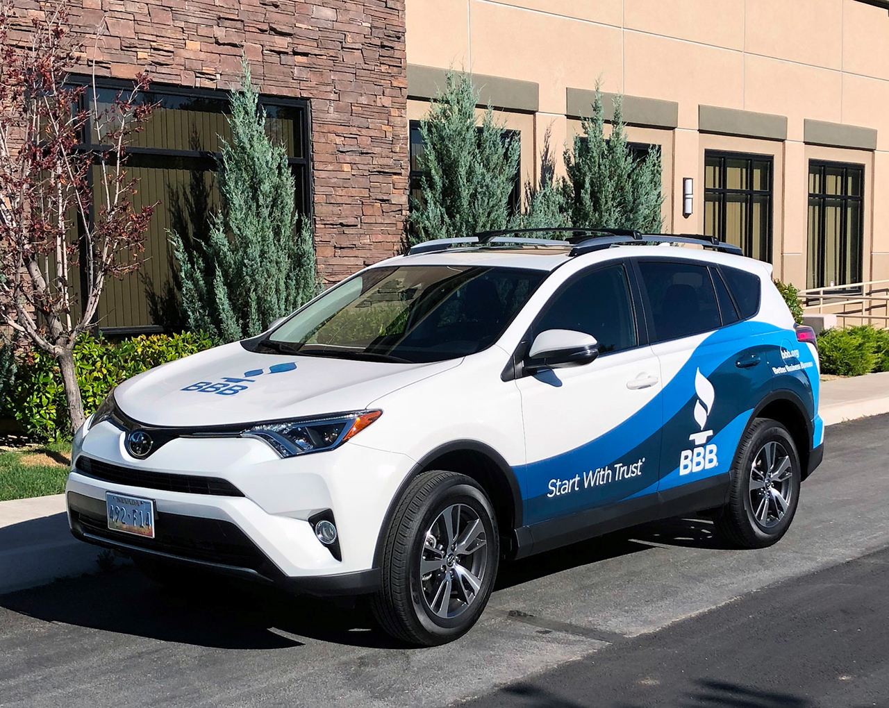 A wrapped car with BBB logo and slogans in front of an office building.