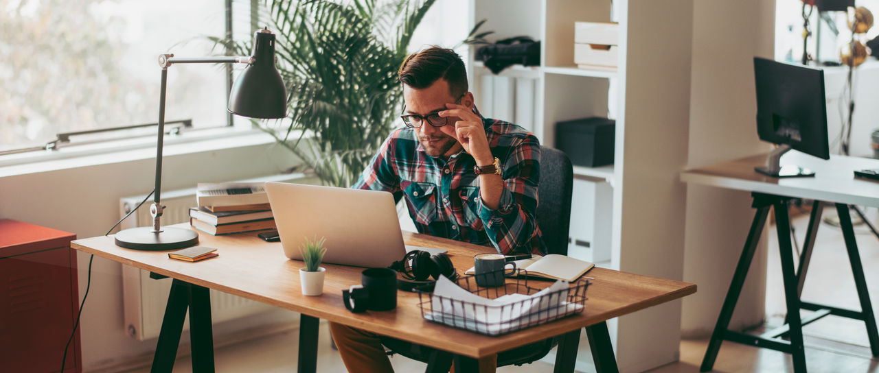 Man using laptop in his office. Shallow DOF. Developed from RAW; retouched with special care and attention; Small amount of grain added for best final impression. 16 bit Adobe RGB color profile.