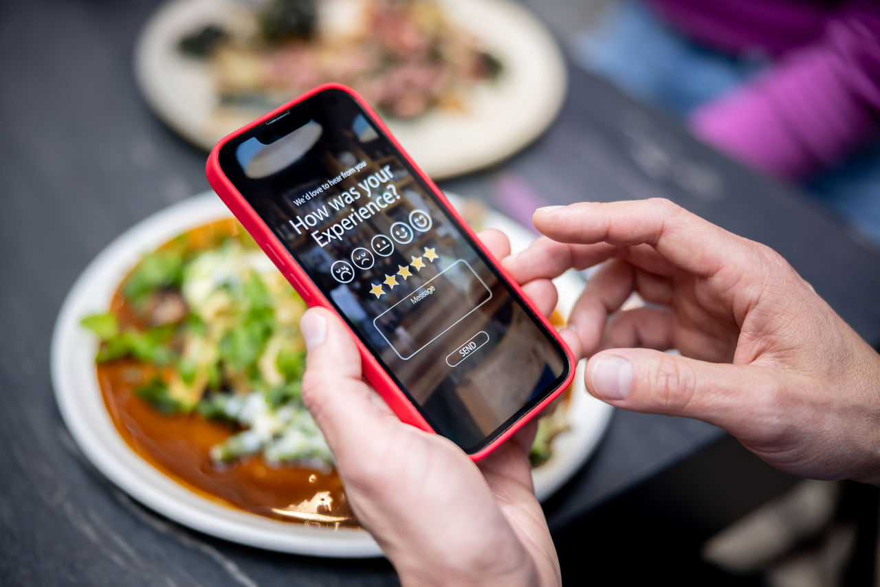 1409730717 Close-up on a man rating his experience at a restaurant using an app on a cell phone - technology concepts